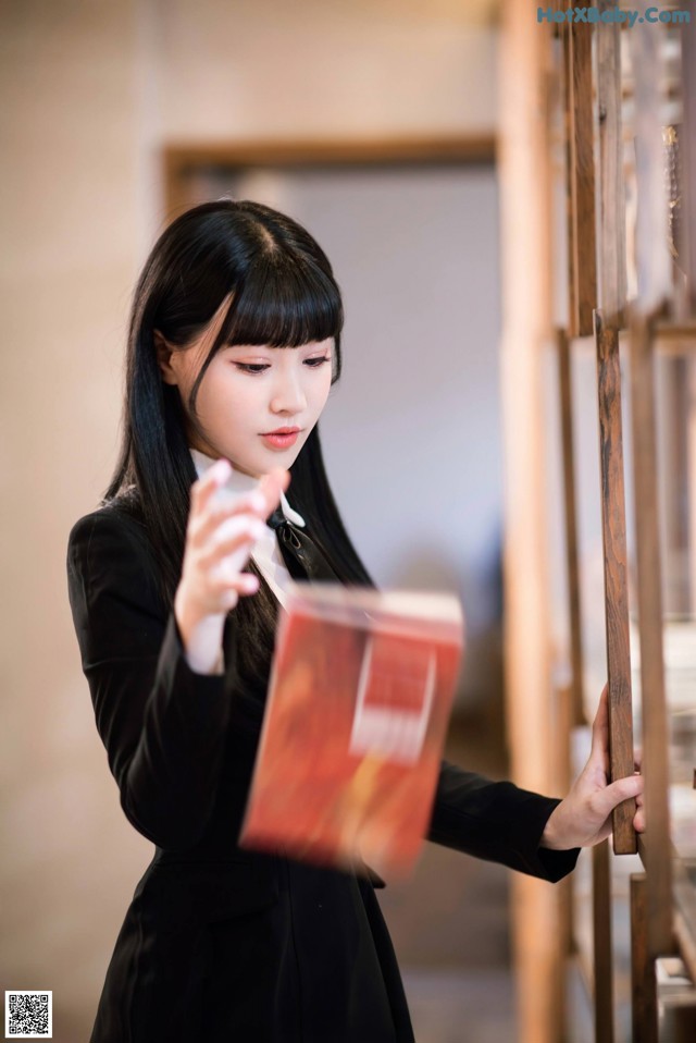 A woman in a black dress holding a red book.