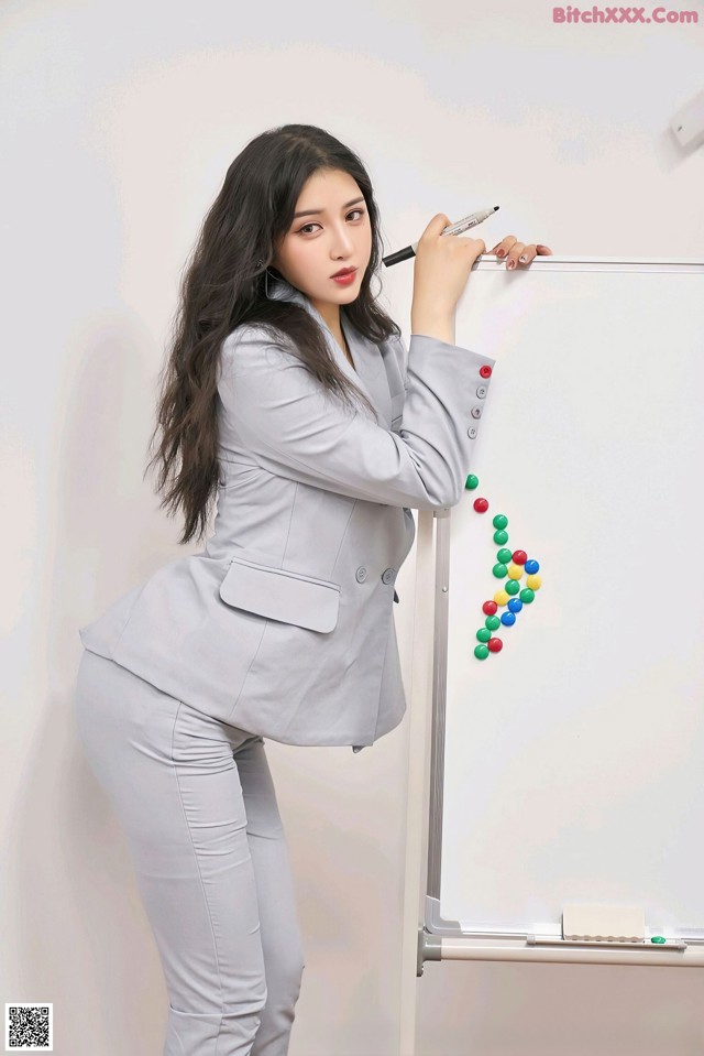 A woman in a gray suit writing on a whiteboard.