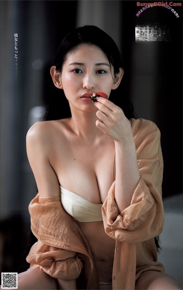 A woman in a white bra top eating a piece of food.