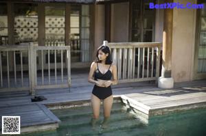 A woman in a black dress standing next to a pool.