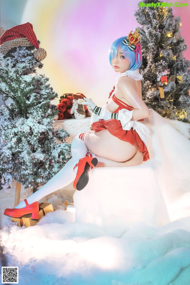 A woman sitting on top of a snow covered ground next to a Christmas tree.