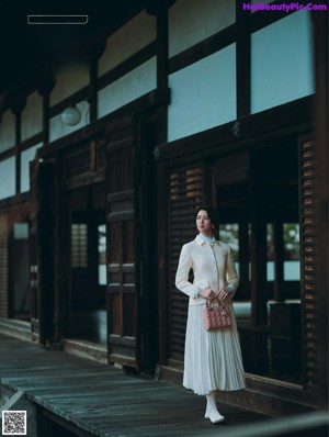 A woman in a white coat is walking by a lake.