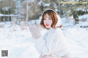 A woman sitting in the snow wearing gloves and a scarf.