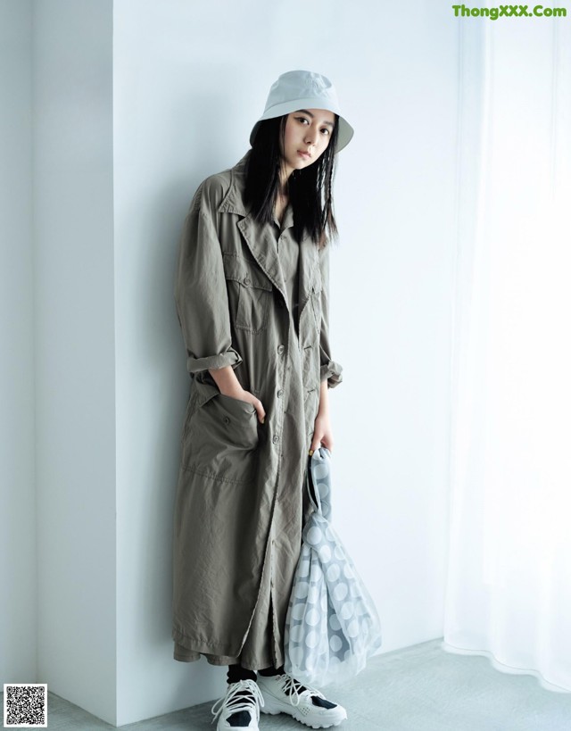 A woman standing in front of a white wall wearing a gray coat and hat.