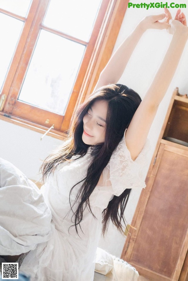 A woman in a white dress stretching on a bed.
