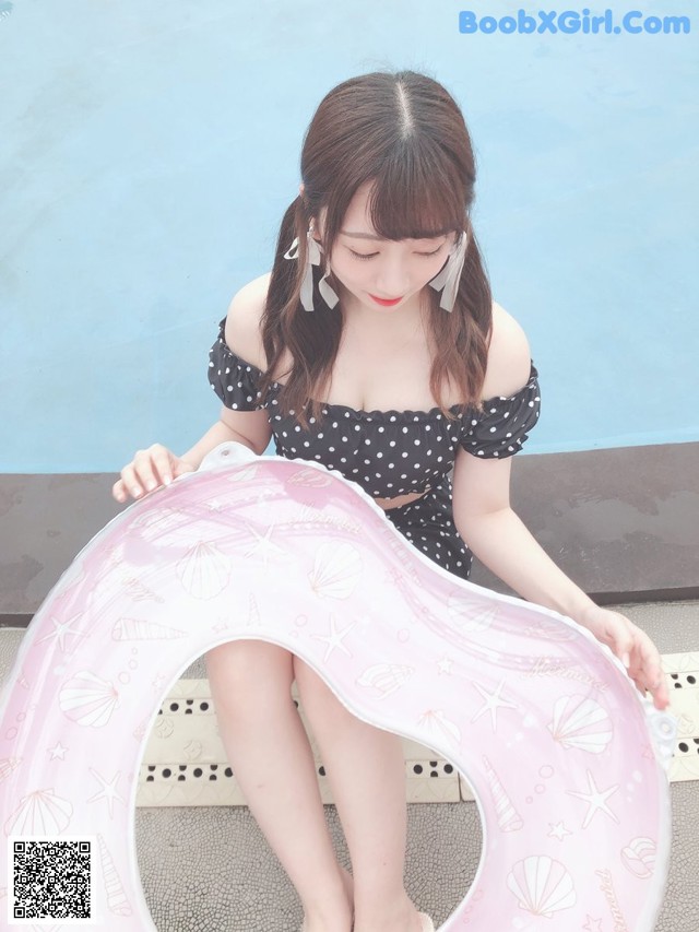 A woman sitting on the edge of a swimming pool holding an inflatable ring.