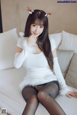 A woman in a white dress sitting on a white couch.