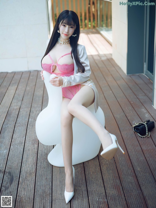 A woman in a pink lingerie sitting on a white chair.