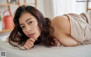 A naked asian woman sitting on a bed.