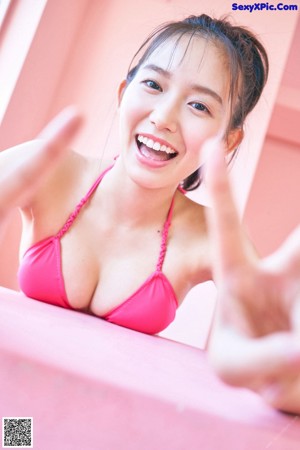 A woman in a pink bikini sitting on a pink wall.
