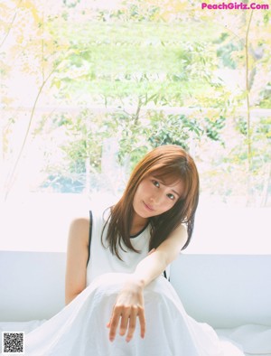 A woman in a white dress sitting on a white couch.