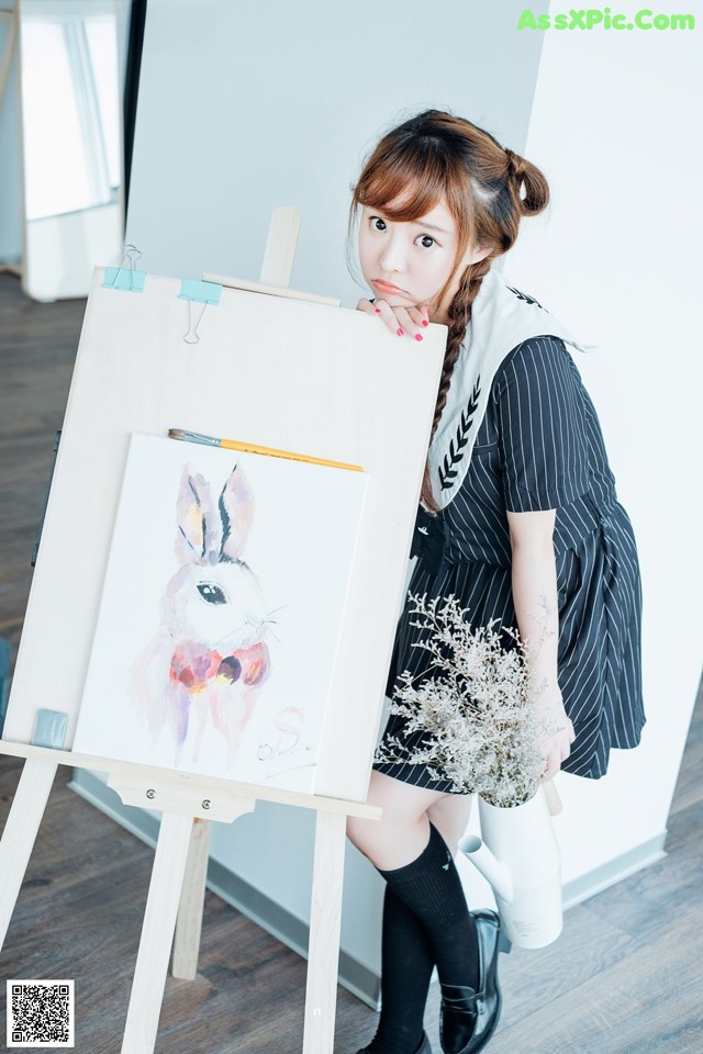 A woman standing next to a painting on a easel.