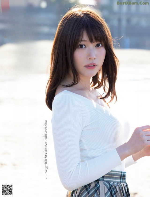 A woman in a white sweater and plaid skirt standing on a beach.