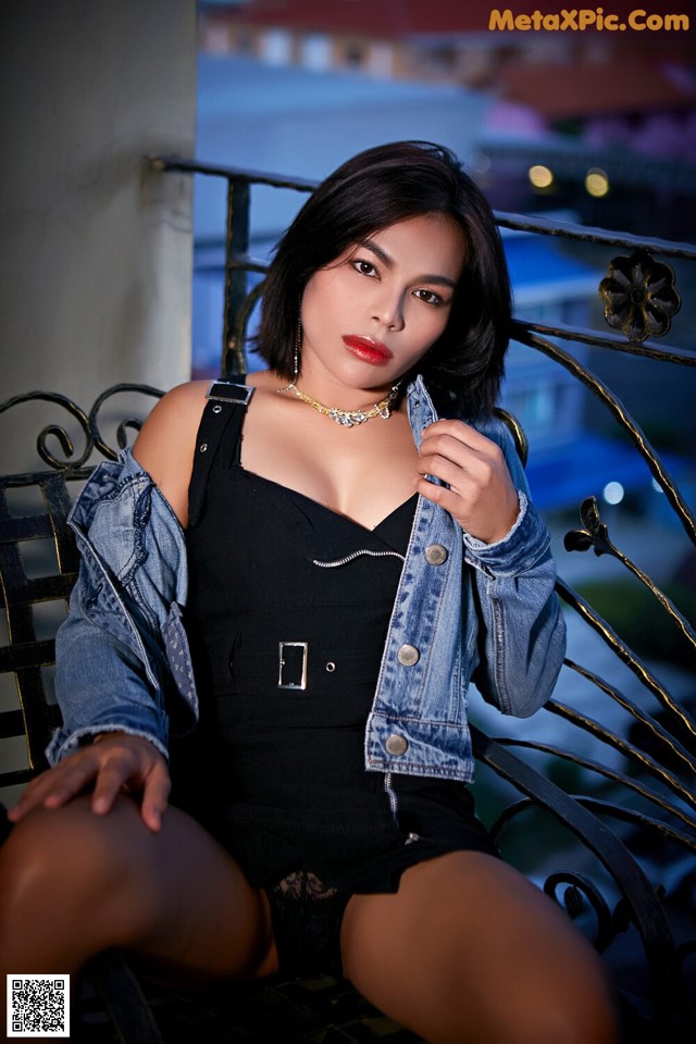 A woman sitting on a bench wearing a denim jacket.