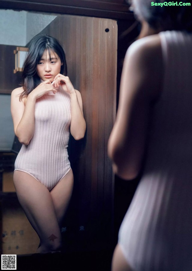 A woman in a white bodysuit standing in front of a mirror.