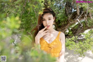 A woman in a yellow top and jeans standing on a beach.