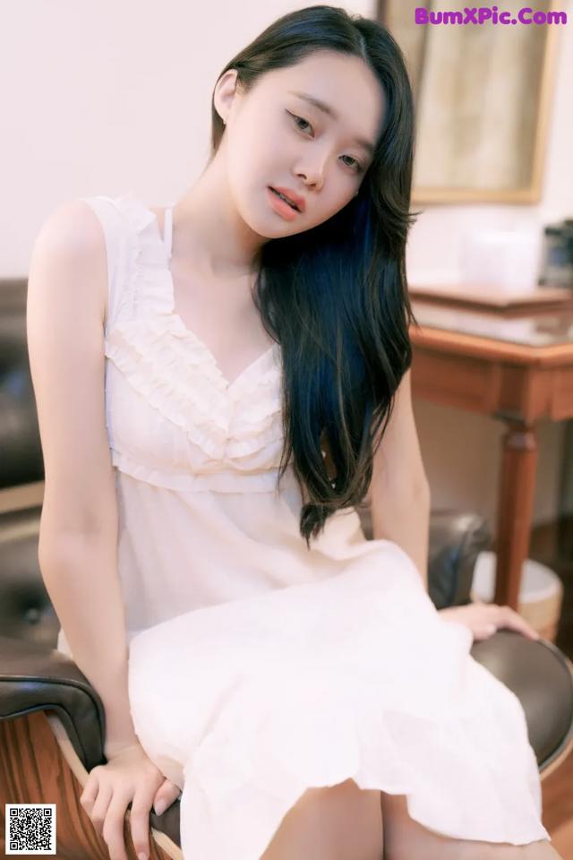 A woman in a white dress sitting on a chair.